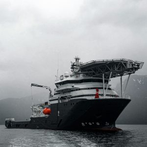 A large offshore vessel navigating through misty Norwegian waters, with mountains in the background.